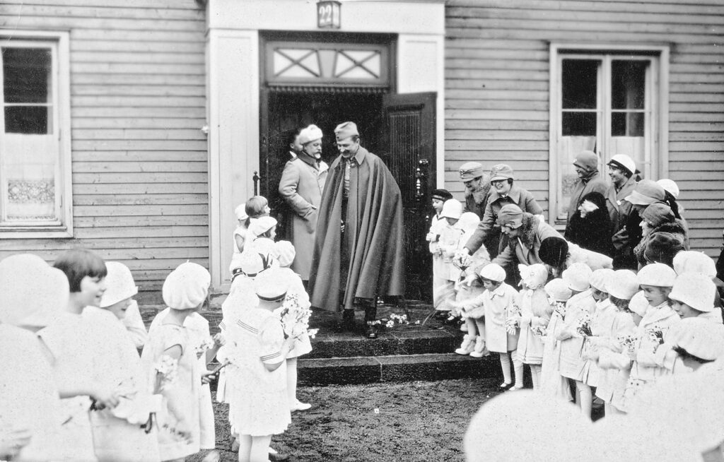 Mannerheim hyllas med blomsterhälsning av unga flickor på trappan framför sitt hus