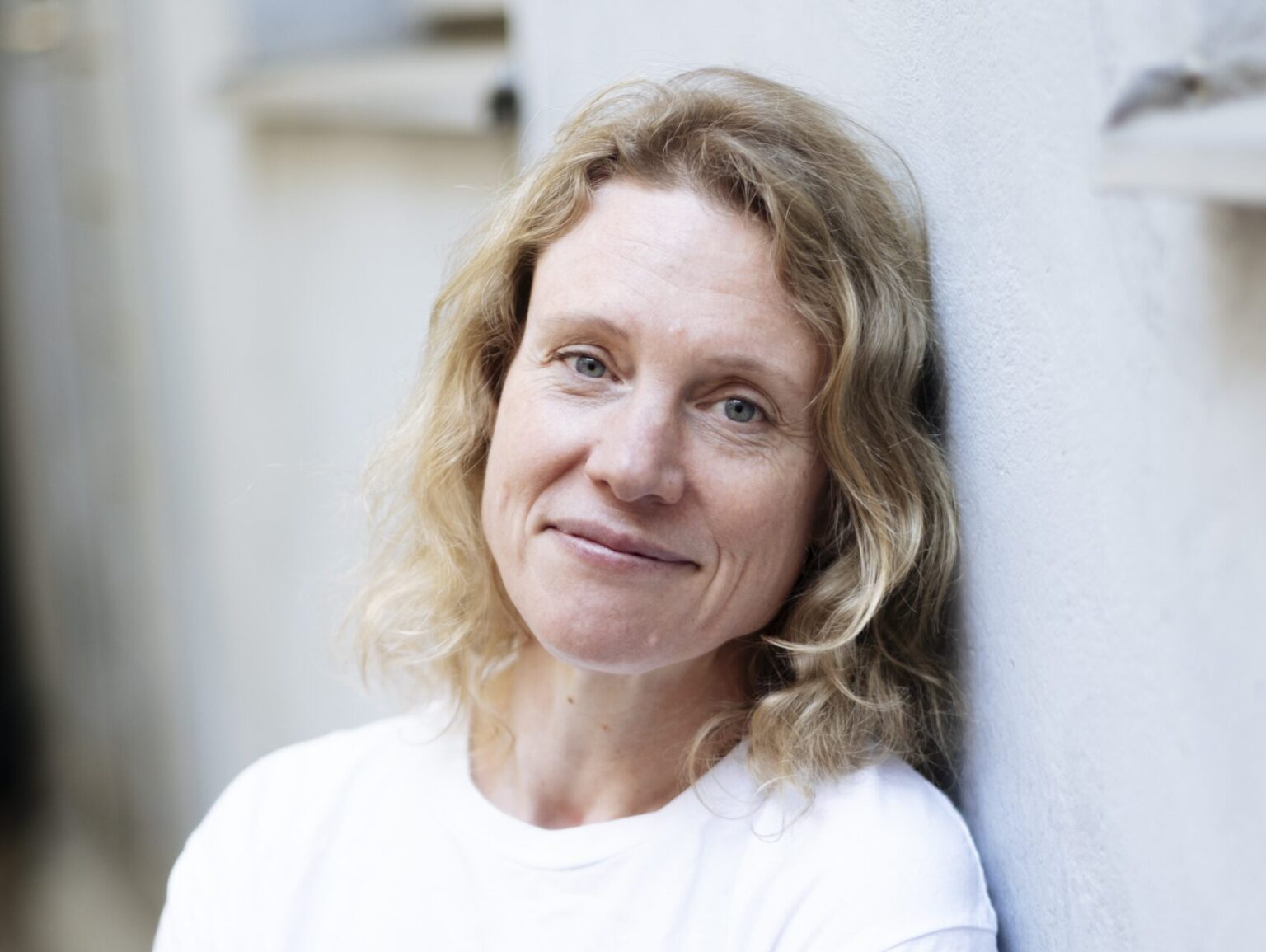 En kvinna i vit t-shirt lutad mot en vägg.